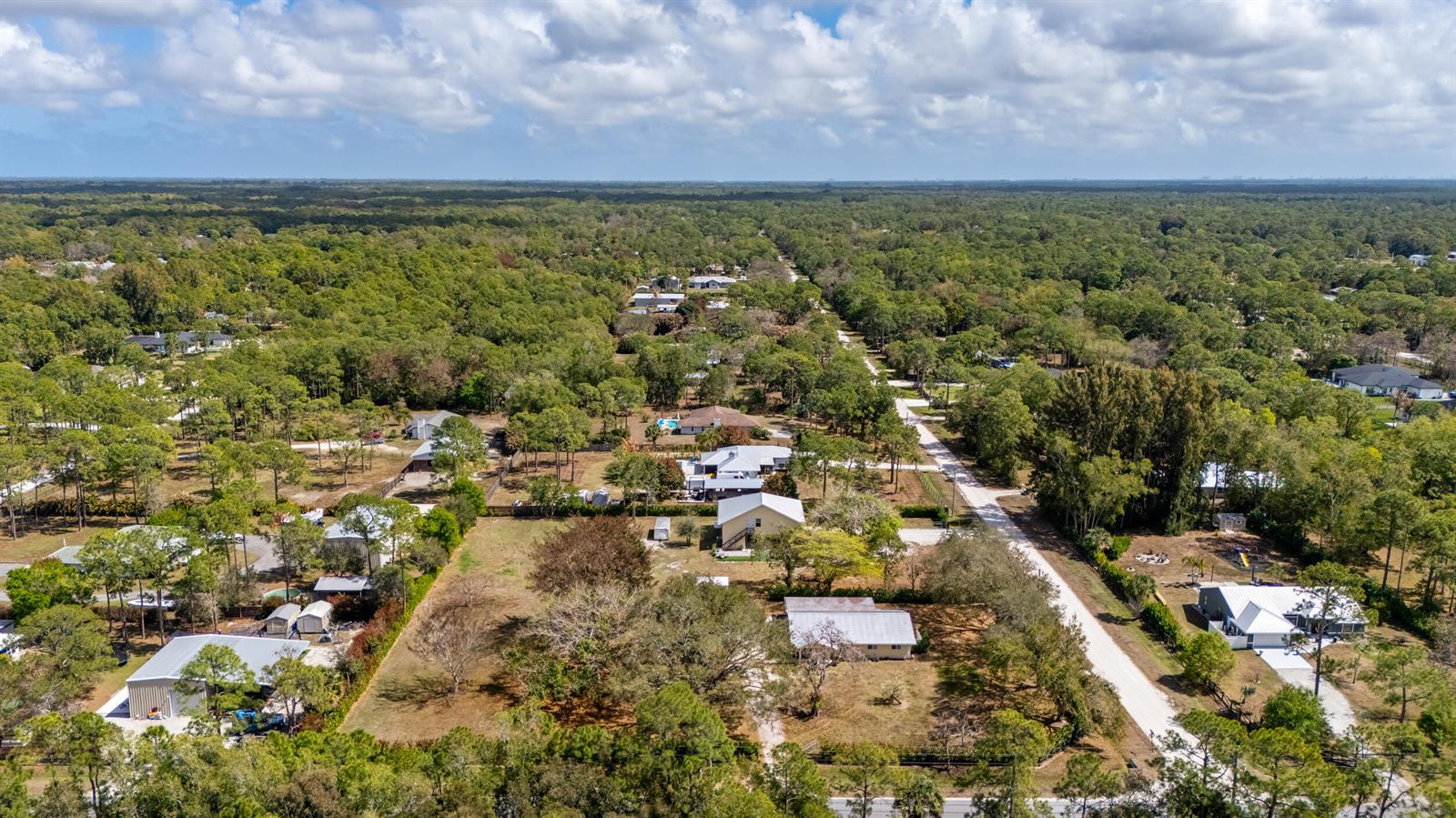 An aerial view shows several houses scattered among dense trees and a dirt road — 15848 N 129th Pl N, FL 33478, FL