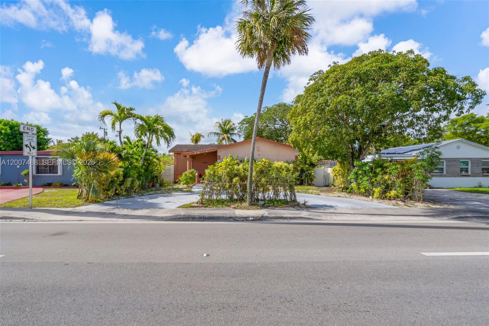 A single-story house with a paved driveway and palm trees sits behind a roadside sign — 1320 NE 135th St, North Miami FL 33161, NORTH MIAMI, FL