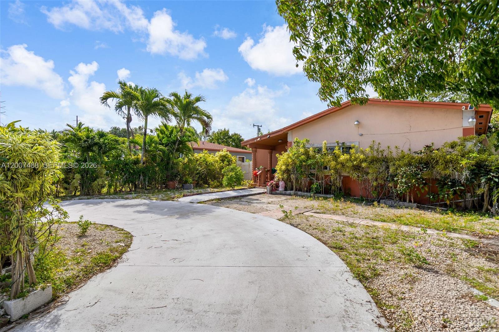 A concrete driveway leads to a single-story house surrounded by palm trees and landscaping — 1320 NE 135th St, North Miami FL 33161, NORTH MIAMI, FL