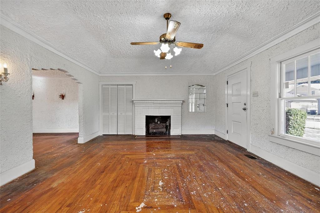 An empty living room features hardwood floors, a white brick fireplace, and a ceiling fan — 5806 N CHEROKEE AVENUE, TAMPA, FL