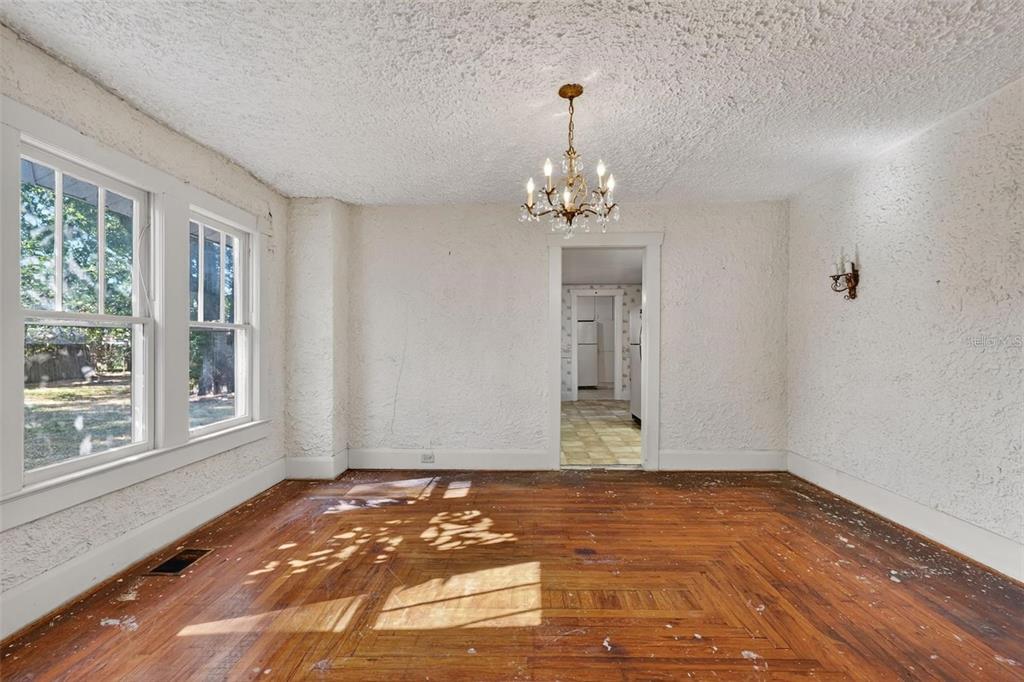 An empty room with hardwood floors, textured white walls, a chandelier, and a doorway — 5806 N CHEROKEE AVENUE, TAMPA, FL