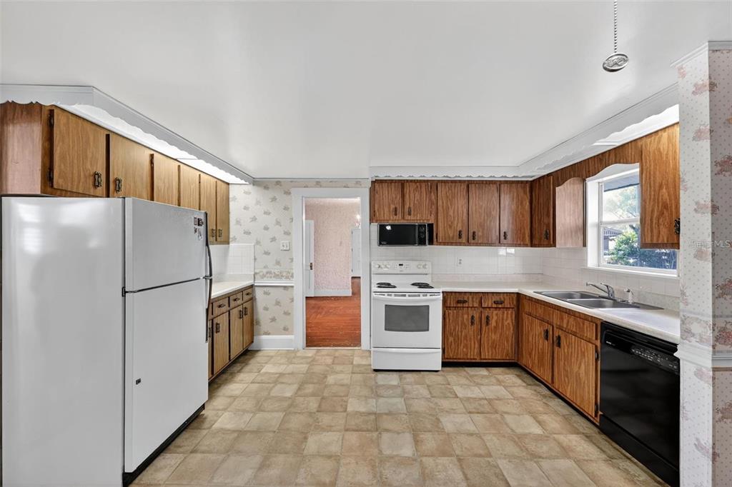 A kitchen with wood cabinets, white appliances, patterned wallpaper, and light-colored square floor tiles — 5806 N CHEROKEE AVENUE, TAMPA, FL