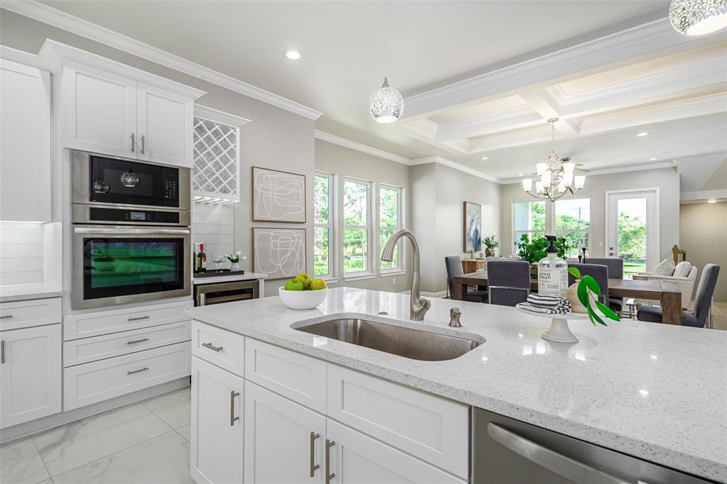 A modern kitchen with white cabinets, quartz countertops, and a stainless steel sink overlooks a dining area — 3847 SEENA MANOR COURT, TAMPA, FL
