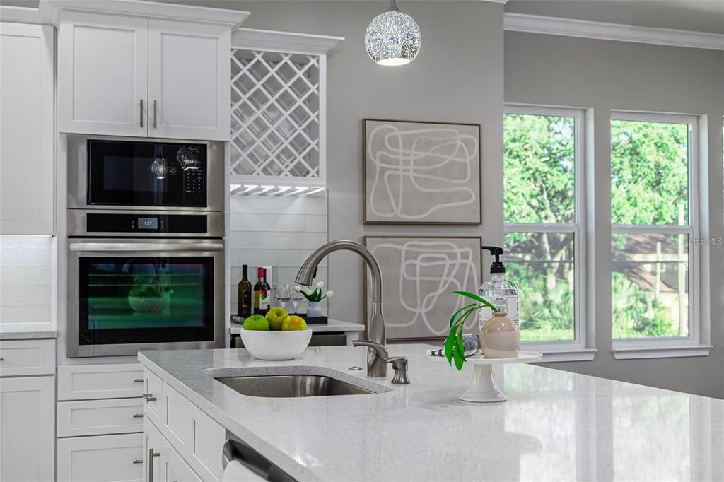 A modern kitchen features white cabinetry, a quartz island countertop, stainless steel appliances, and windows — 3847 SEENA MANOR COURT, TAMPA, FL