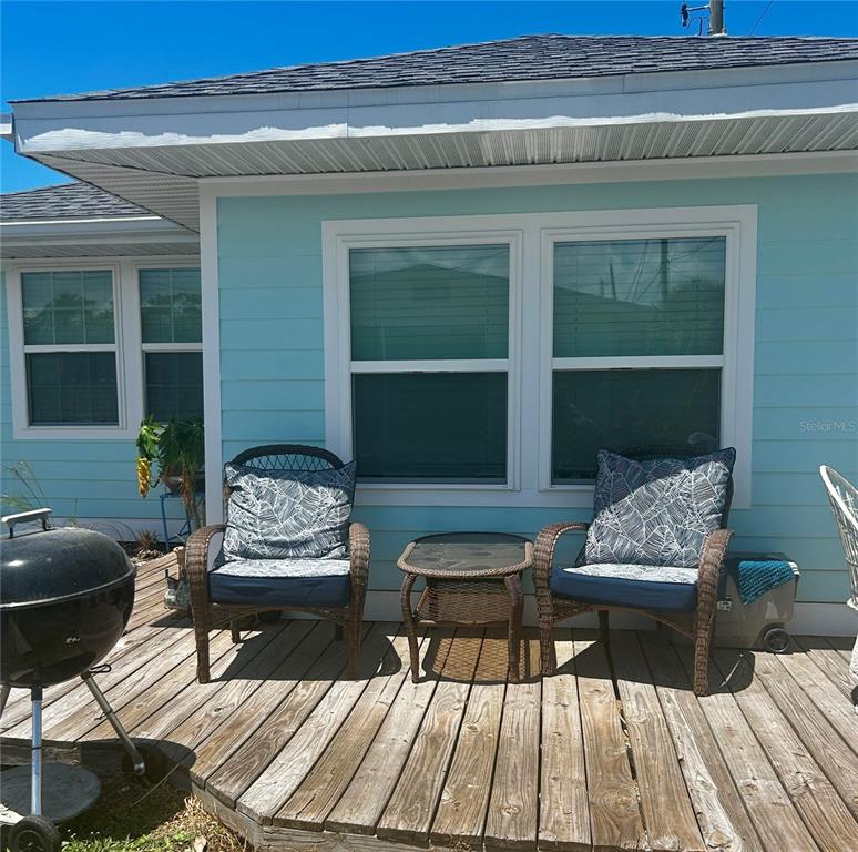 A wooden deck features two wicker chairs with patterned cushions and a small side table — 470 S MCCALL ROAD UNIT 8, ENGLEWOOD, FL