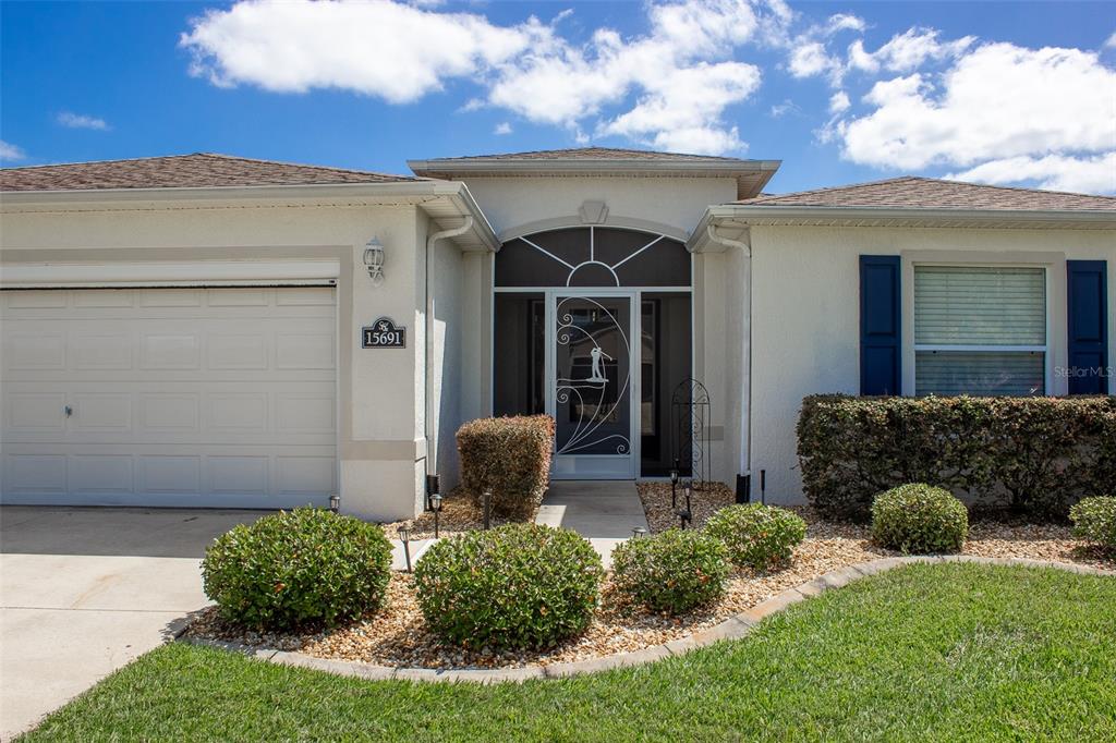 A single-story house exterior features a two-car garage, a front entryway with a screen door, and landscaping — 15691 SW 11TH COURT ROAD, OCALA, FL