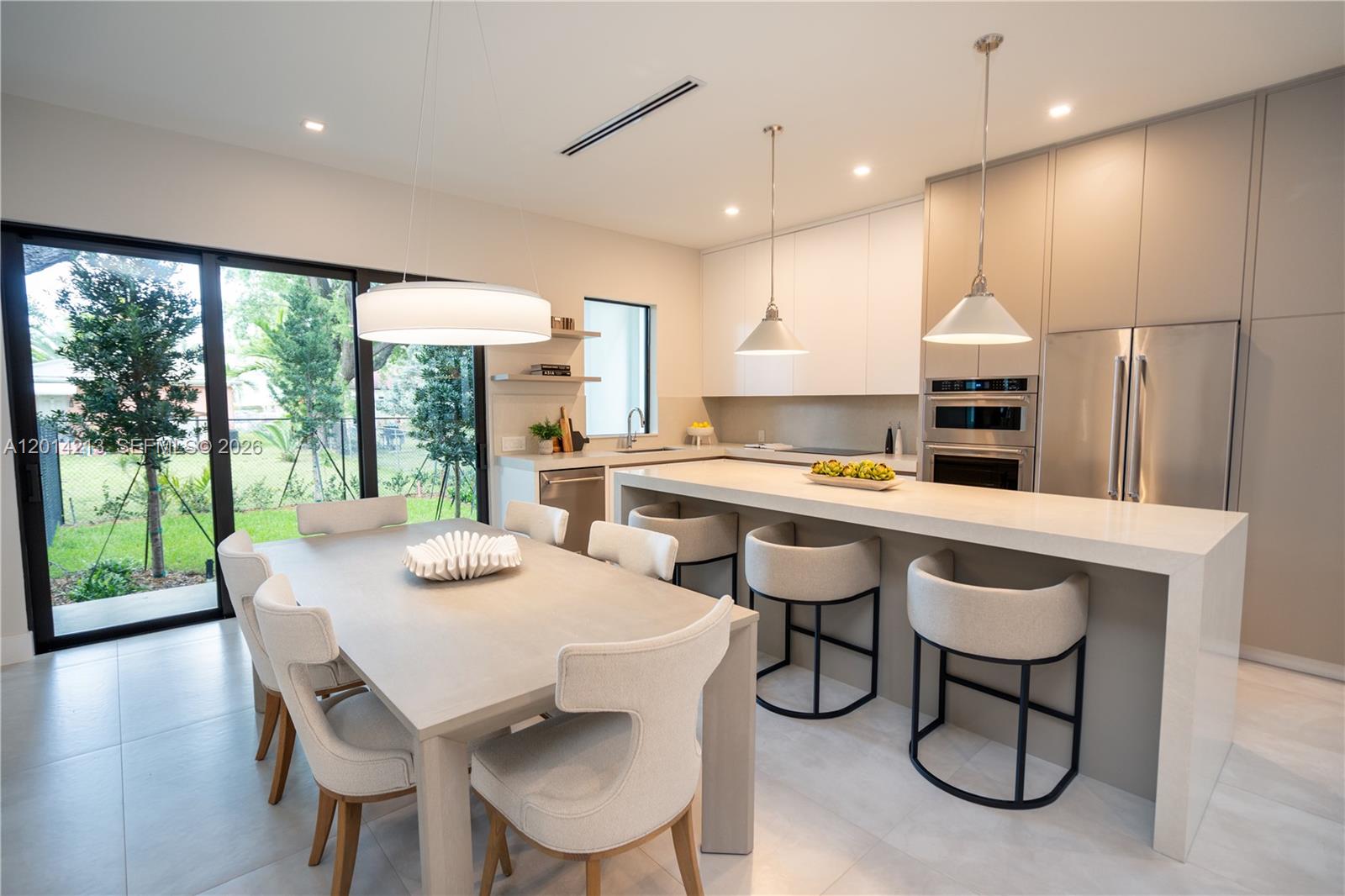 A modern kitchen and dining area features a large island, neutral cabinetry, and sliding glass doors — 2745 SW 23 Ter, Miami FL 33145, MIAMI, FL
