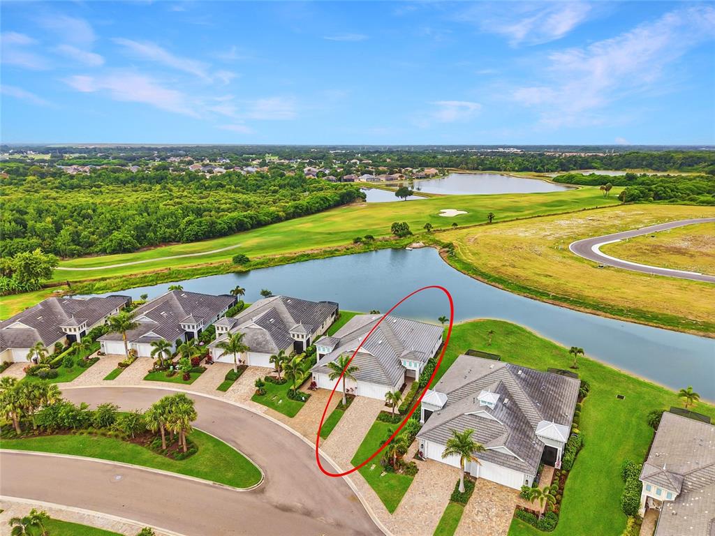 An aerial view shows a residential house with a tiled roof near a lake — 132 VAN GOGH COVE, BRADENTON, FL