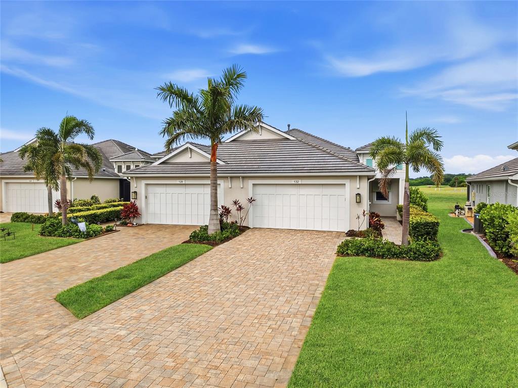 The exterior view shows a duplex with two garage doors, paver driveways, and palm trees — 132 VAN GOGH COVE, BRADENTON, FL