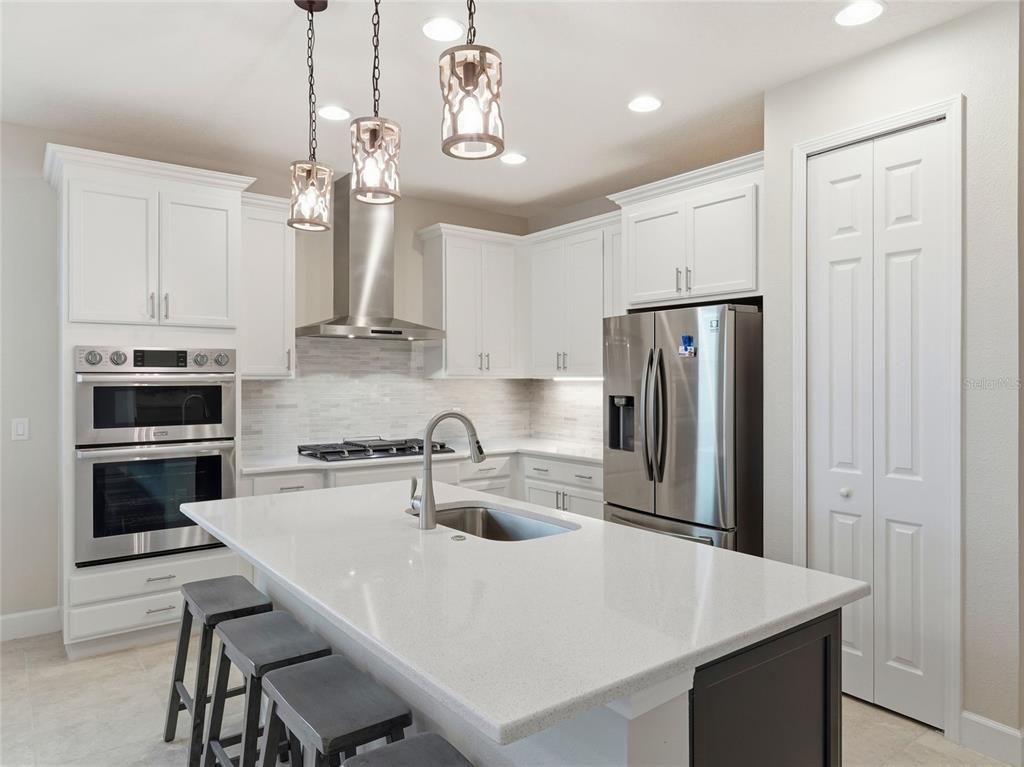 A modern kitchen features white cabinetry, stainless steel appliances, a quartz island, and pendant lighting — 132 VAN GOGH COVE, BRADENTON, FL