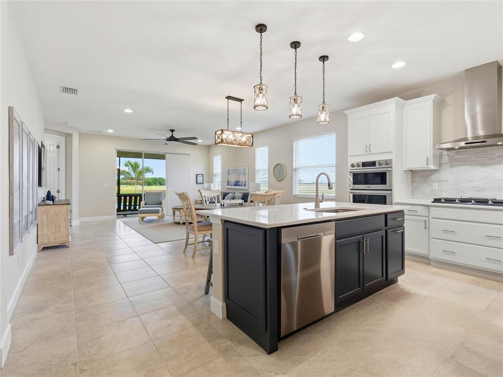 A kitchen with a dark island and white cabinets opens to a dining and living area — 132 VAN GOGH COVE, BRADENTON, FL