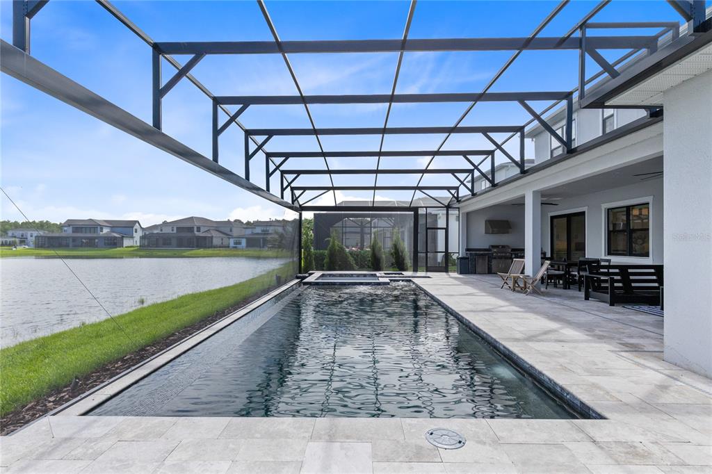 A screened-in patio features a rectangular swimming pool, a spa, and a view of a lake — 9445 SANTORINI DRIVE, ORLANDO, FL