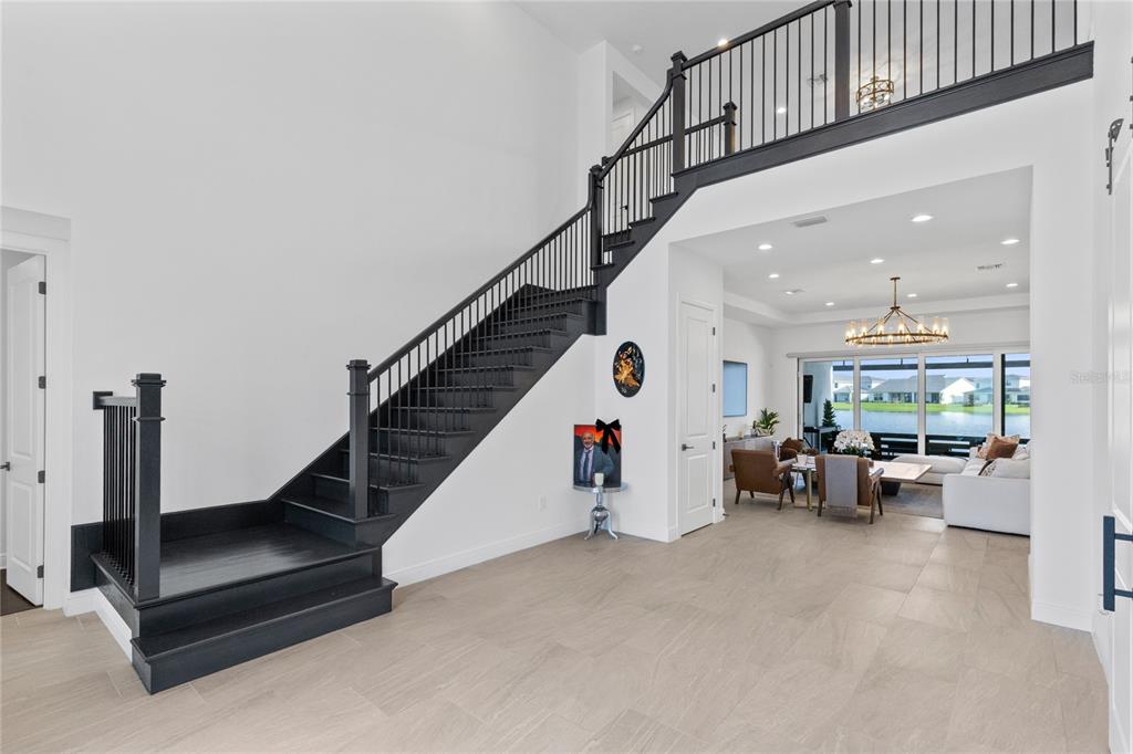 A foyer with light tile flooring features a black staircase leading to an upper landing — 9445 SANTORINI DRIVE, ORLANDO, FL