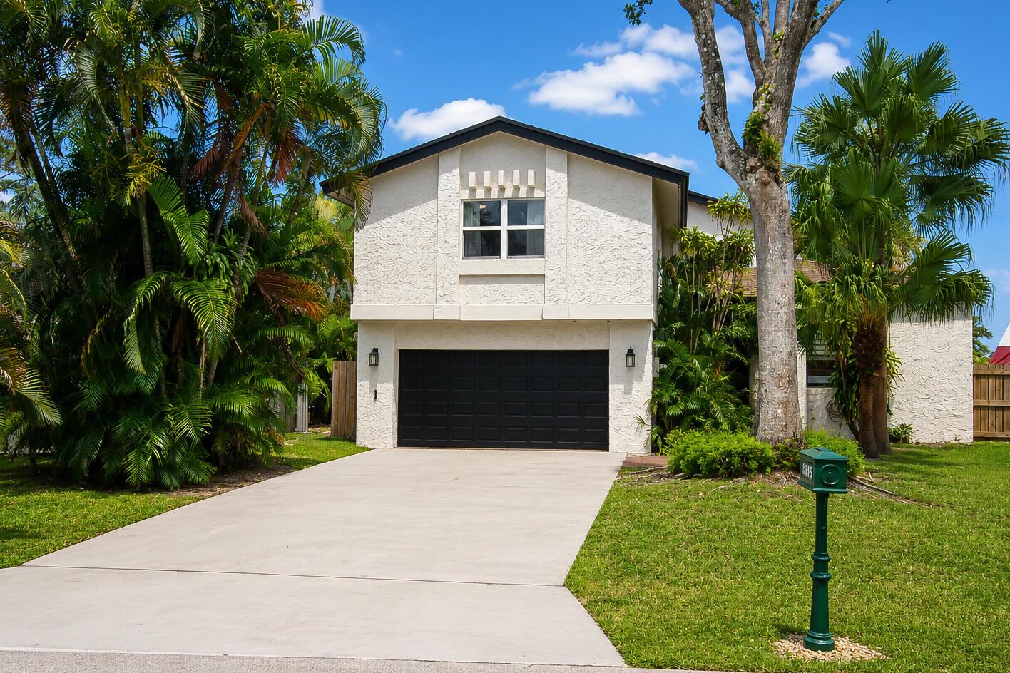 A two-story house with a black garage door and white stucco exterior sits behind a driveway — 6458 Pond Apple Road, Boca Raton FL 33433, BOCA RATON, FL