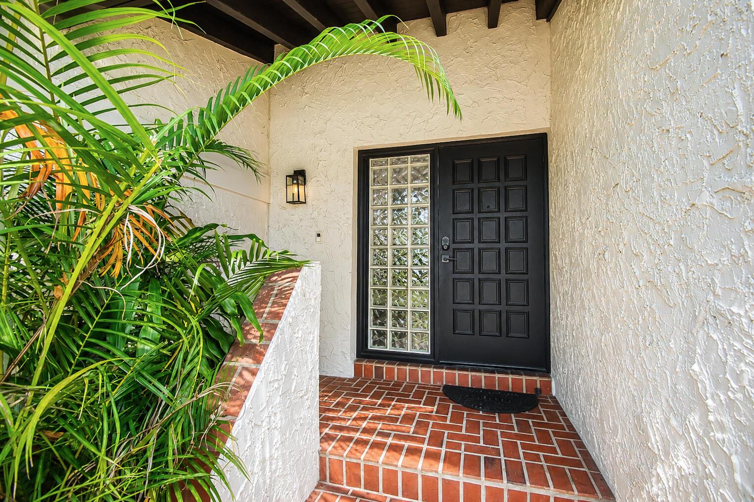 A black front door with glass blocks sits on a brick porch by a plant — 6458 Pond Apple Road, Boca Raton FL 33433, BOCA RATON, FL