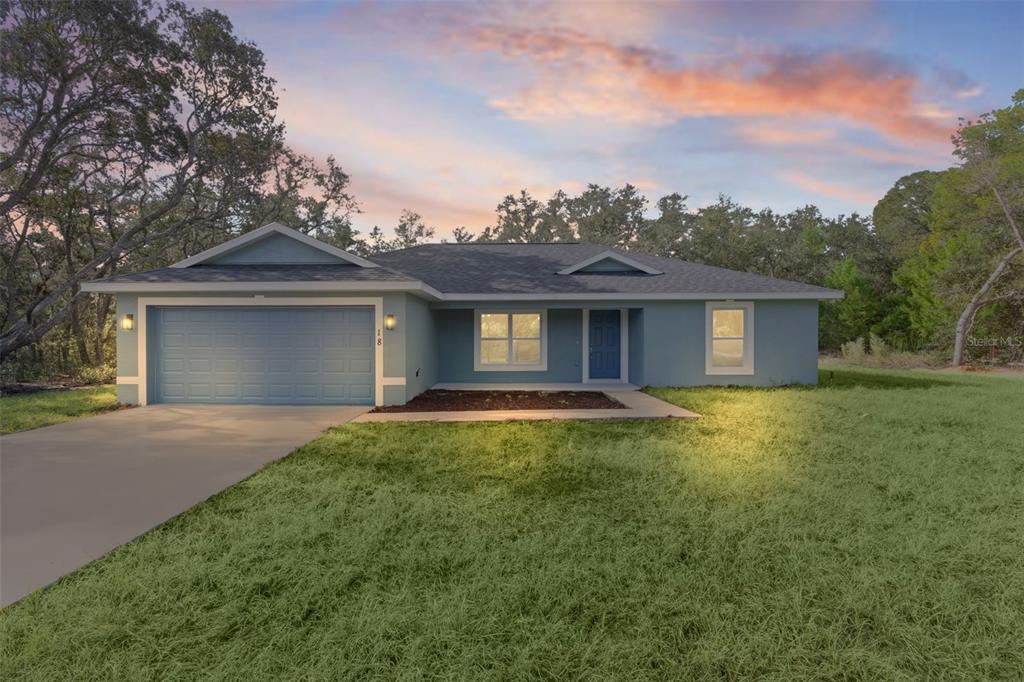 A single-story blue house with a two-car garage and a concrete driveway at sunset — 18 FISHER TERRACE WAY, OCKLAWAHA, FL