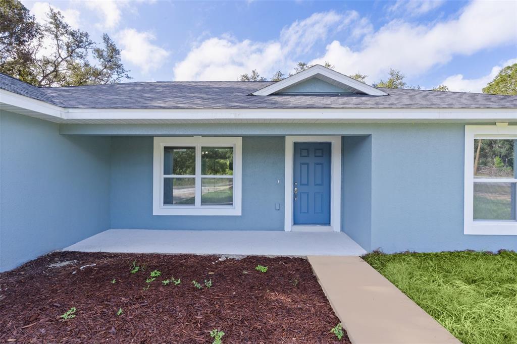 A light blue house exterior features a covered porch, a blue front door, and windows — 18 FISHER TERRACE WAY, OCKLAWAHA, FL