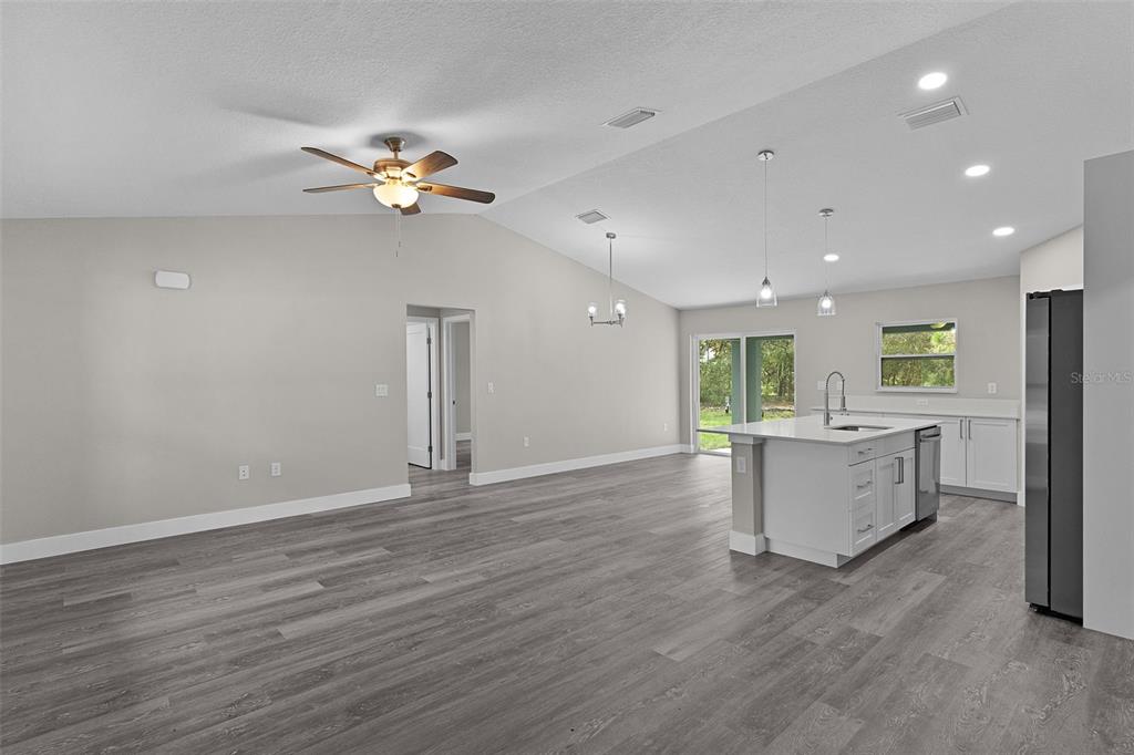 An open-concept kitchen and living area features gray wood-look flooring and a central island — 18 FISHER TERRACE WAY, OCKLAWAHA, FL