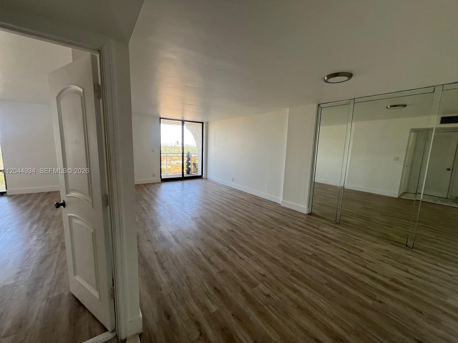 An empty room features wood-look flooring, mirrored closet doors, and a sliding glass balcony door — 1600 S Ocean Dr # 18C, Hollywood FL 33019, HOLLYWOOD, FL