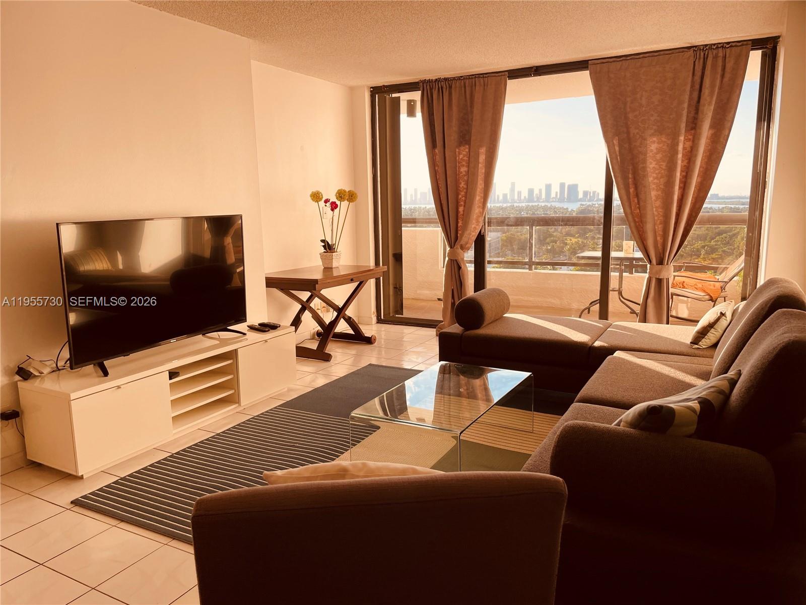 A living room features a television, sofa, glass coffee table, and a balcony with views — 2555 Collins Ave # 1804, Miami Beach FL 33140, MIAMI BEACH, FL