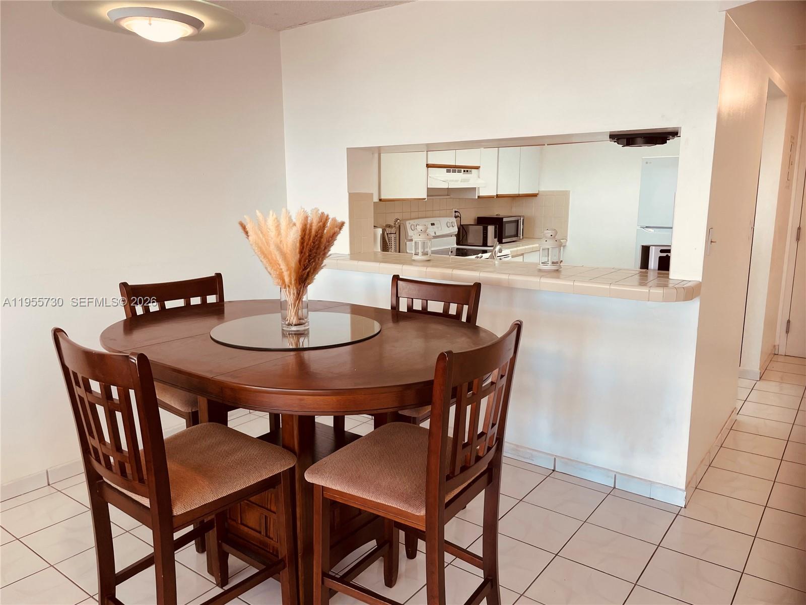A dining area with a round wooden table and chairs sits before a kitchen pass-through window — 2555 Collins Ave # 1804, Miami Beach FL 33140, MIAMI BEACH, FL
