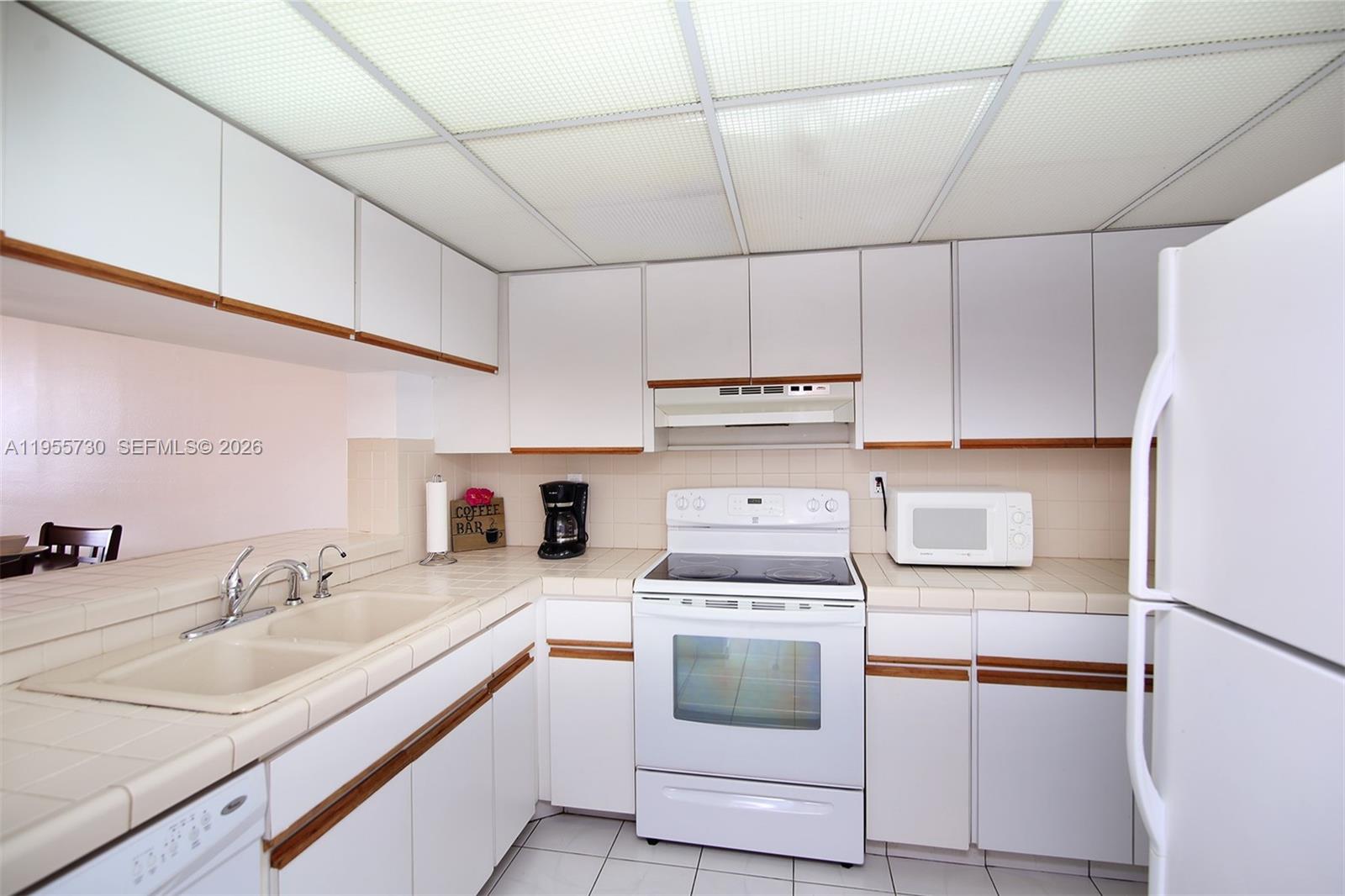 A kitchen features white cabinets with wood trim, tiled countertops, and a drop ceiling — 2555 Collins Ave # 1804, Miami Beach FL 33140, MIAMI BEACH, FL