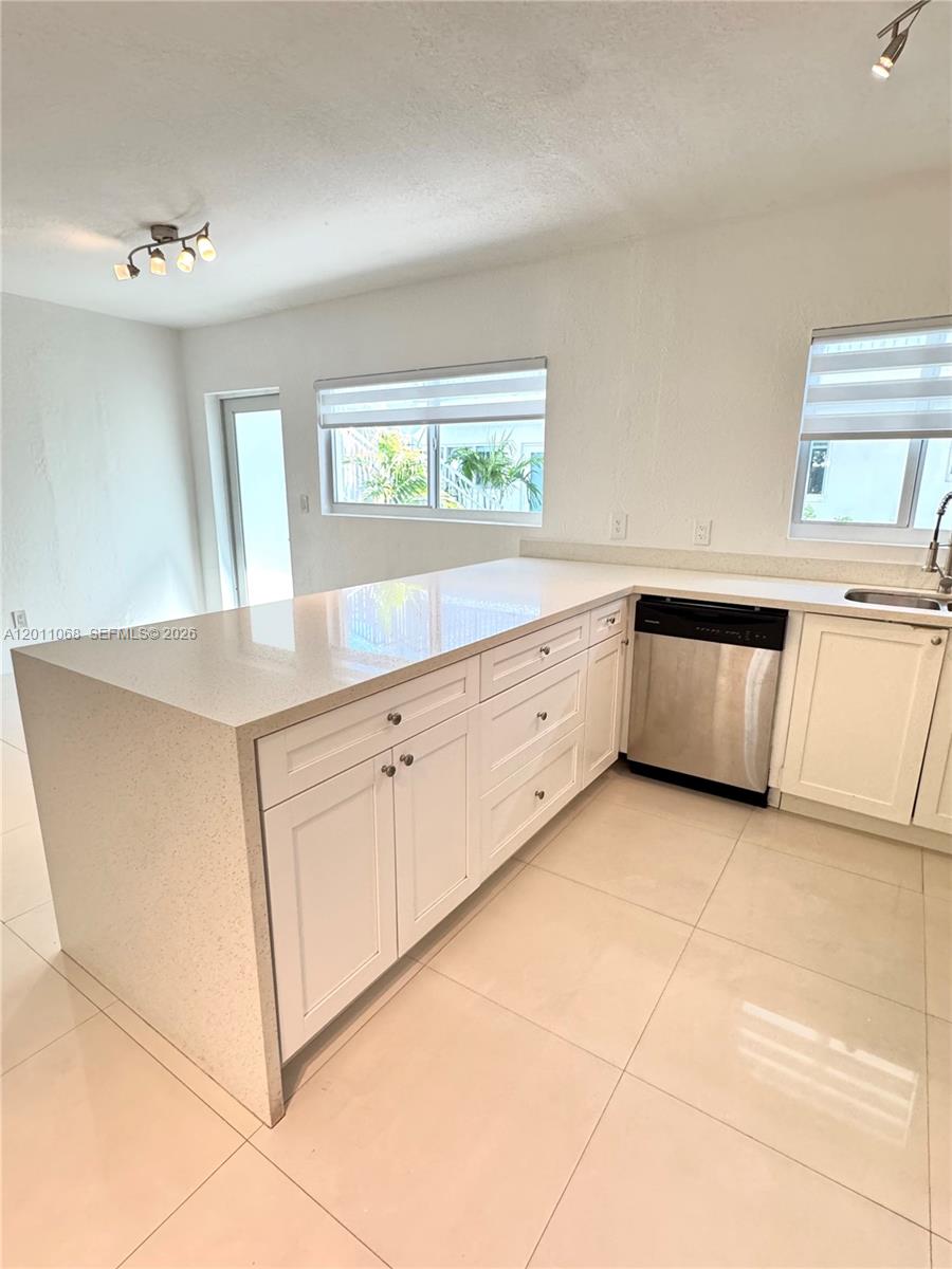 A kitchen features white cabinets, a quartz countertop, and a stainless steel dishwasher — 8035 Crespi Blvd # 9, Miami Beach FL 33141, MIAMI BEACH, FL