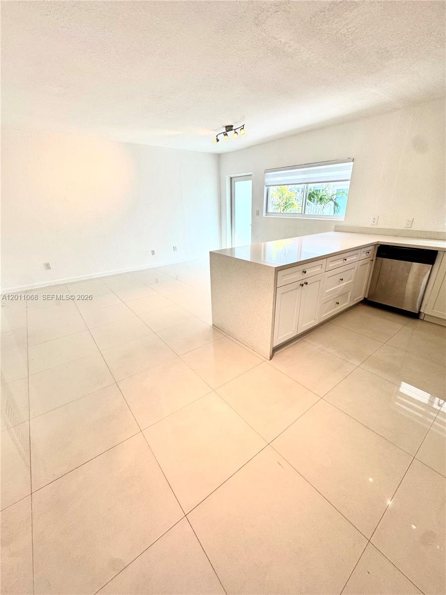 A kitchen with white cabinets and a peninsula overlooks an open-concept living area — 8035 Crespi Blvd # 9, Miami Beach FL 33141, MIAMI BEACH, FL