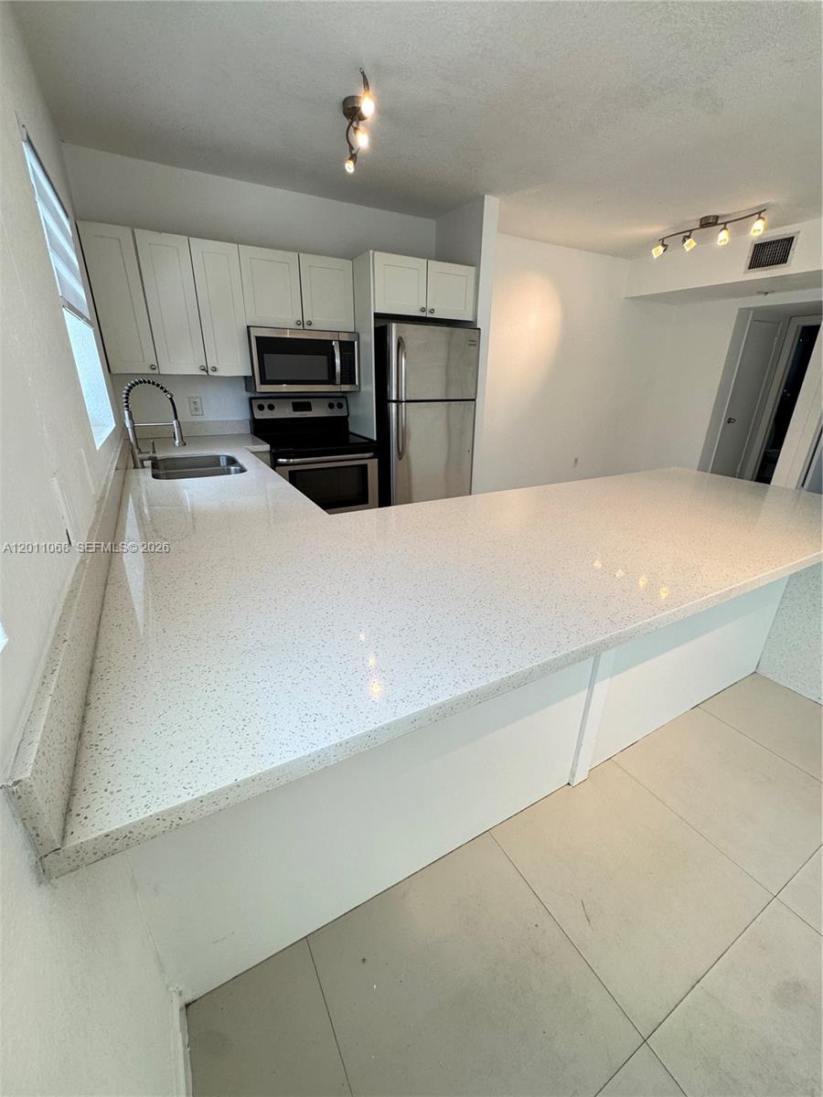 A kitchen features white cabinets, stainless steel appliances, and a white quartz breakfast bar — 8035 Crespi Blvd # 9, Miami Beach FL 33141, MIAMI BEACH, FL