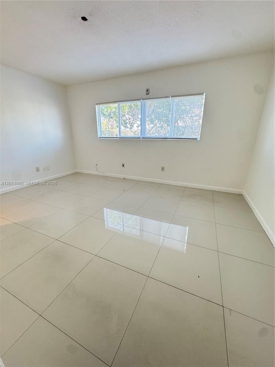 An empty room features white walls, large light-colored floor tiles, and a window with blinds — 8035 Crespi Blvd # 9, Miami Beach FL 33141, MIAMI BEACH, FL