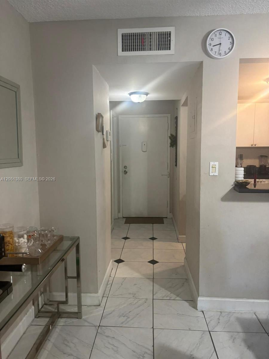 A hallway with white tiled floors leads to a front door under a ceiling light — DEERFIELD BEACH, FL