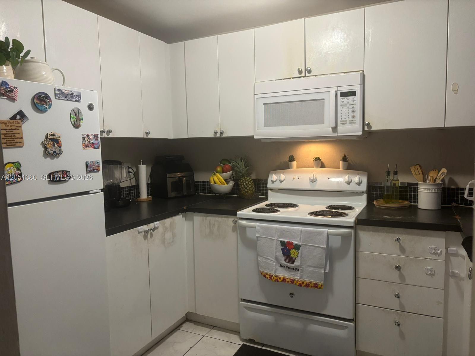 A kitchen with white cabinets, black countertops, white appliances, and a tiled backsplash — DEERFIELD BEACH, FL