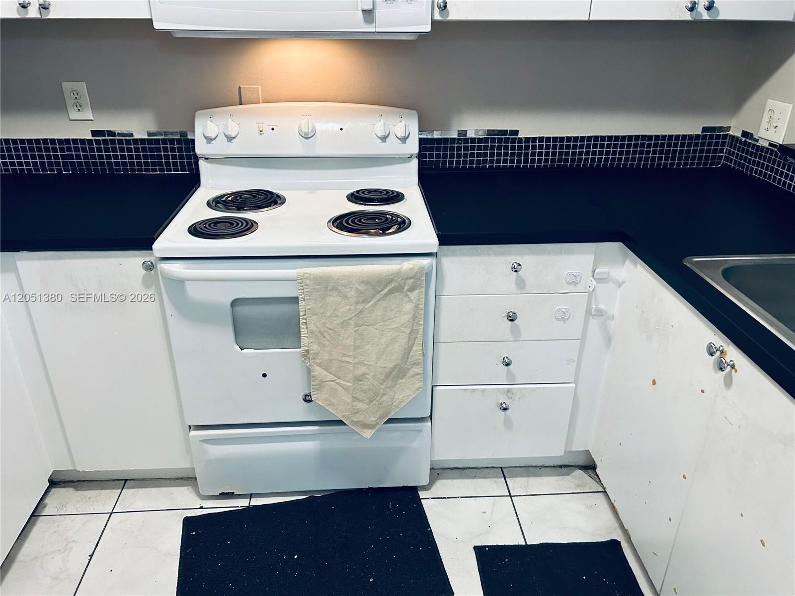 A white electric stove sits between black countertops and white cabinets in a kitchen — DEERFIELD BEACH, FL