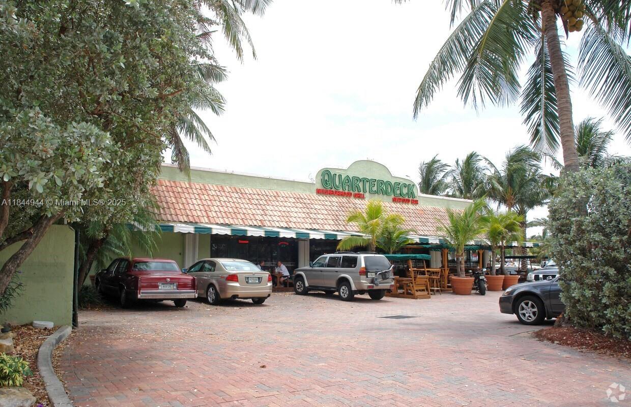 A brick parking lot sits in front of a Quarterdeck restaurant with palm trees — FORT LAUDERDALE, FL