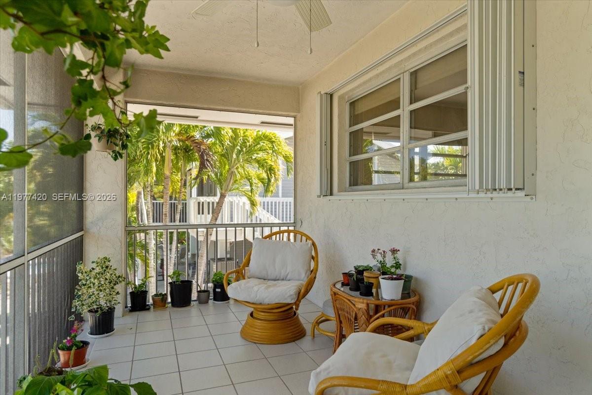 A screened-in balcony features tiled flooring, two wicker chairs, and several potted plants — 29051 Magnolia Ln, Big Pine FL 33043, BIG PINE, FL