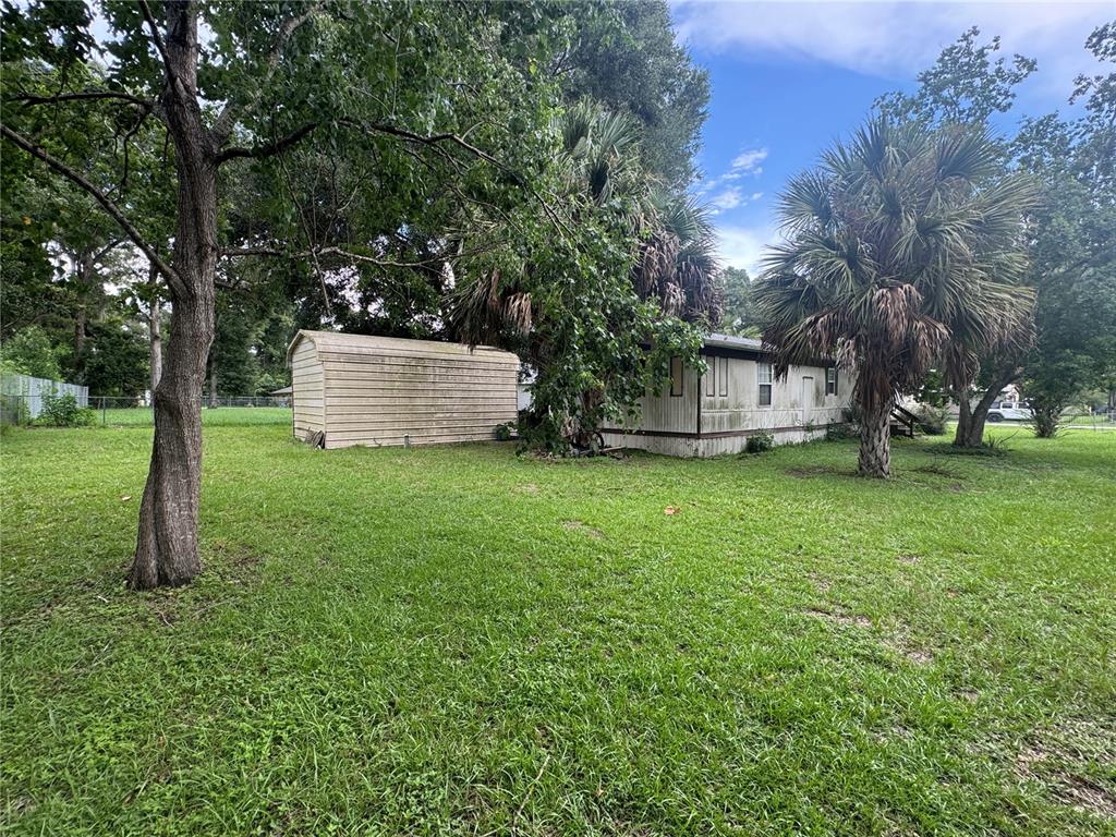 A mobile home and a detached metal shed sit on a grassy, tree-filled lot — 3285 SE 131ST PLACE, BELLEVIEW, FL