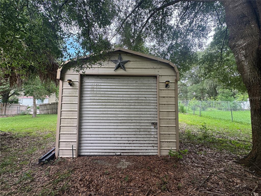 A detached metal storage shed with a roll-up door and a decorative star sits outdoors — 3285 SE 131ST PLACE, BELLEVIEW, FL