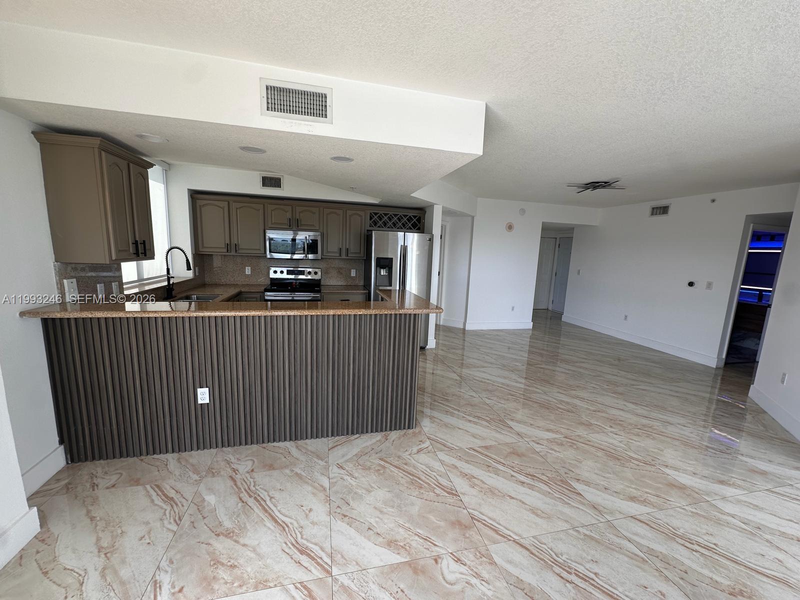 A kitchen with brown cabinets and a breakfast bar overlooks a large, tiled living area — 4242 NW 2nd St # 1116, Miami FL 33126, MIAMI, FL