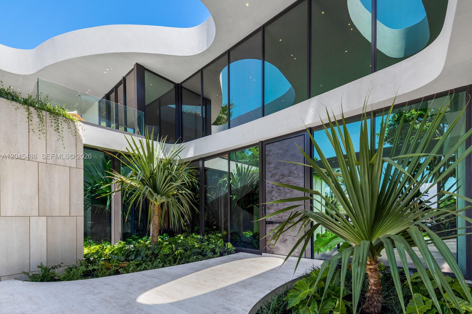 A modern home exterior features a curved white roof, large glass windows, and tropical landscaping — 1015 S Southlake Dr, Hollywood FL 33019, HOLLYWOOD, FL
