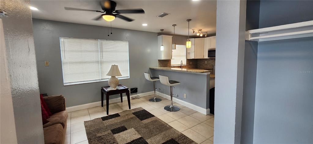 A living room with a ceiling fan, tiled floors, and a breakfast bar kitchen — 10706 N 15TH STREETS UNIT A, TAMPA, FL