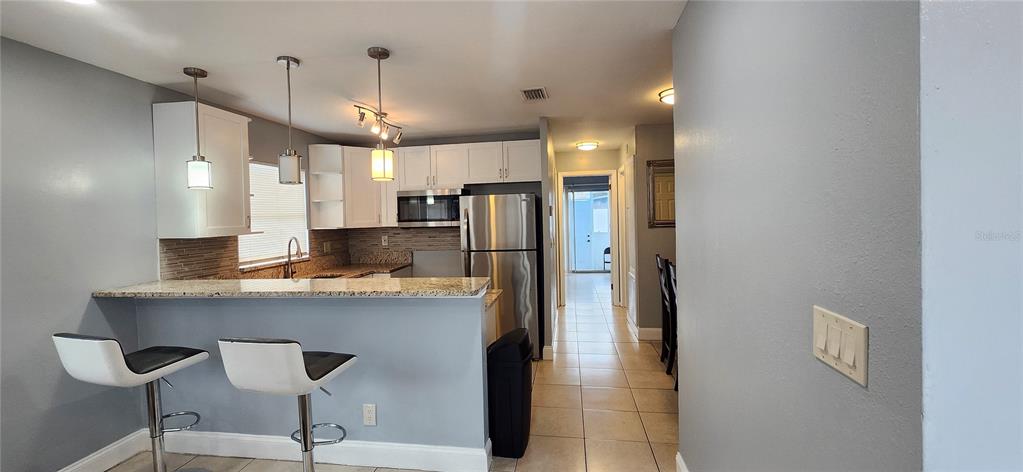 A kitchen with white cabinets, stainless steel appliances, a granite breakfast bar, and tile flooring — 10706 N 15TH STREETS UNIT A, TAMPA, FL