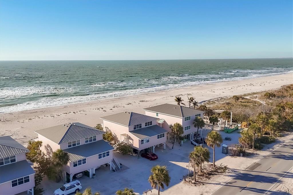 An aerial view shows three pink beach houses situated along a sandy coastline — 290 GULF BOULEVARD UNIT 17, BOCA GRANDE, FL