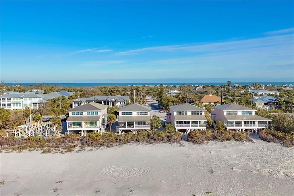 An aerial view shows four elevated beach houses situated along a sandy shoreline — 290 GULF BOULEVARD UNIT 17, BOCA GRANDE, FL