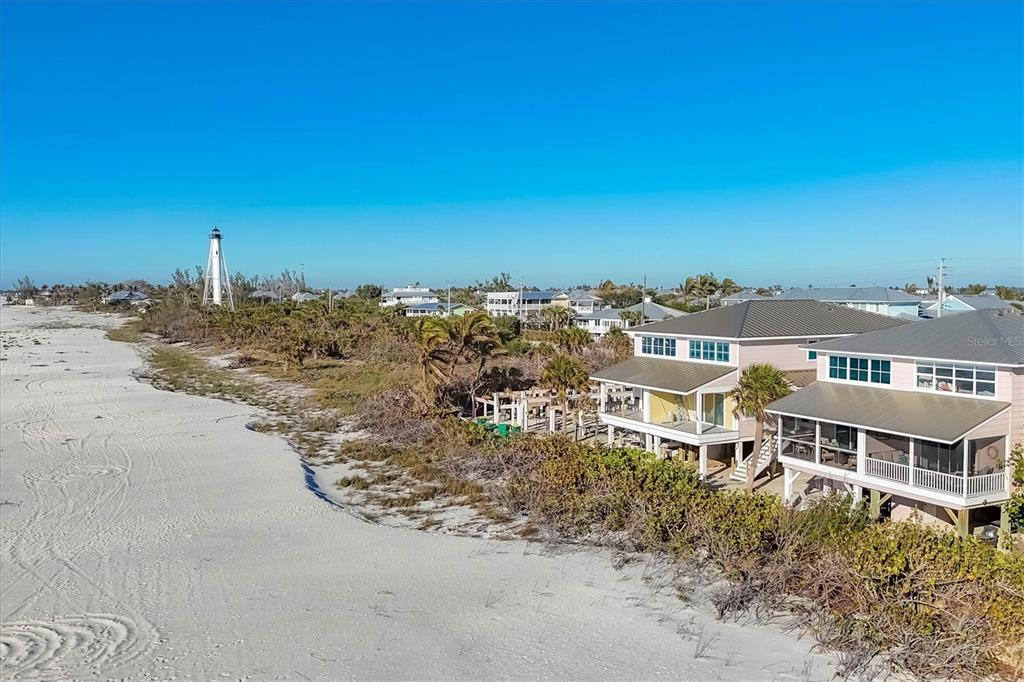 A white lighthouse stands near a sandy beach and elevated coastal houses — 290 GULF BOULEVARD UNIT 17, BOCA GRANDE, FL
