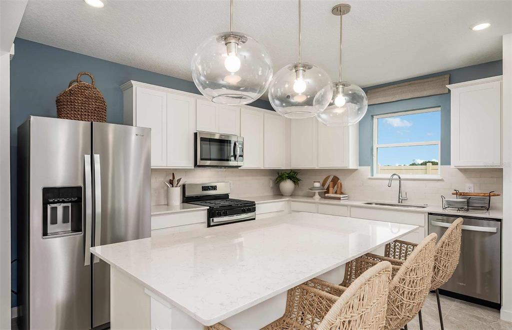 A kitchen features white cabinets, a large quartz island, stainless steel appliances, and globe pendant lights — 9147 NEWMONS PLACE, WILDWOOD, FL