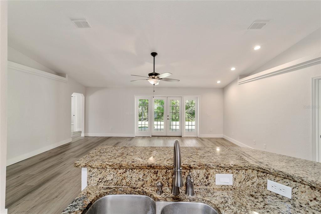 A kitchen sink with granite countertops overlooks a living area with wood-look flooring and doors — 4020 NE 14TH COURT, OCALA, FL