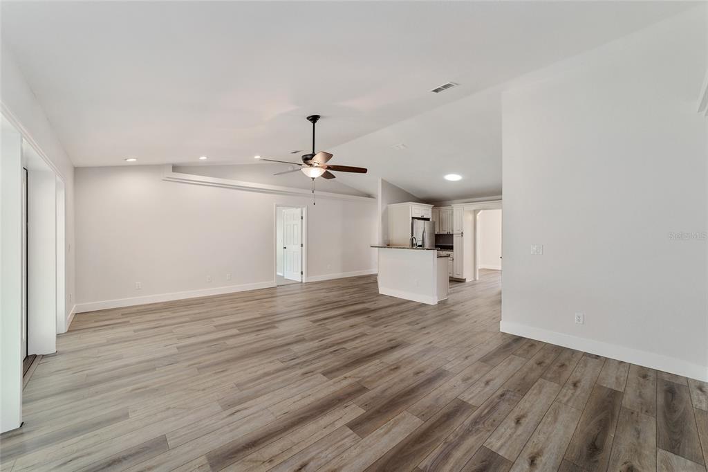 An open-concept living area features light wood-look flooring, a vaulted ceiling, and a kitchen island — 4020 NE 14TH COURT, OCALA, FL