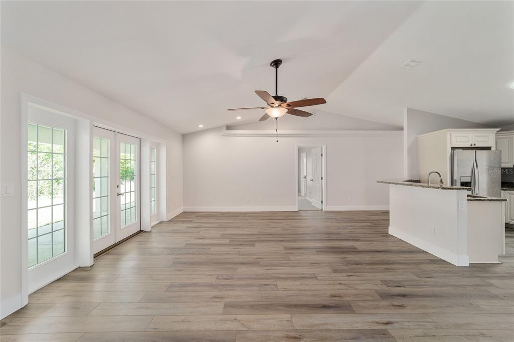 A bright living room features light wood-look flooring, a vaulted ceiling, and a kitchen peninsula — 4020 NE 14TH COURT, OCALA, FL