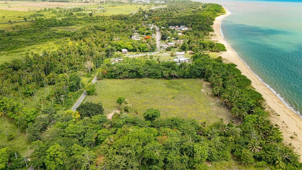 An aerial view shows a large, grassy plot of land bordered by trees and the ocean — COMM. PLAYA, CARR. 401 KM. HM 1.9, ANASCO, PR