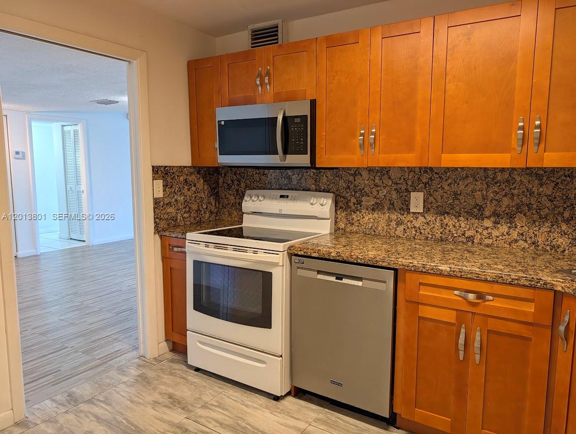 A kitchen features wood cabinets, granite countertops, a white stove, and a stainless steel dishwasher — 210 Sea View Dr # 405, Key Biscayne FL 33149, KEY BISCAYNE, FL